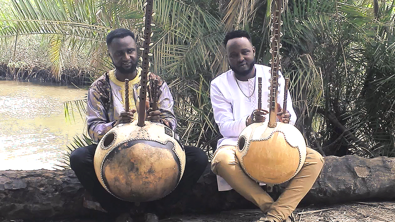 Two musicians pose outside near a river with their instruments