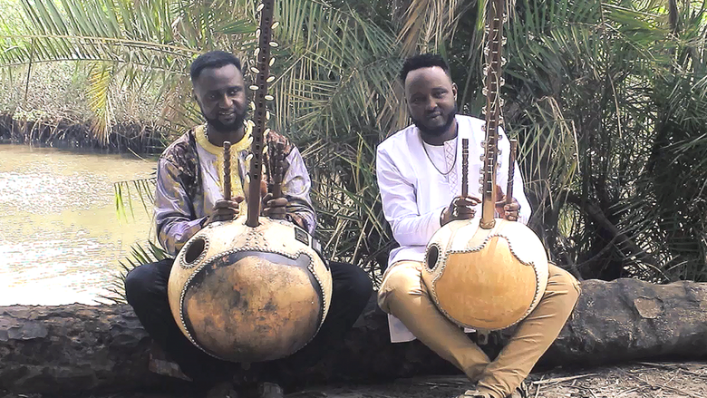 Two musicians pose outside near a river with their instruments