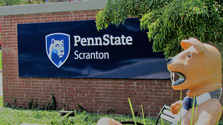 nittany lion mascot sitting on bench at campus entrance sign