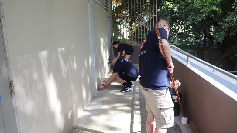 students painting the outside railing and walkway of a building