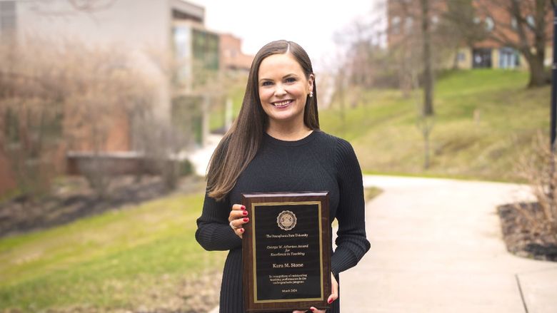 Kara Stone poses outside fo the library building with her award plaque