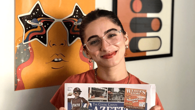 A student wearing glasses holds up an issue of the Gazette newspaper