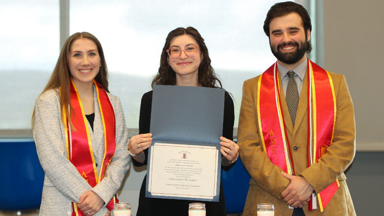 New lambda pi eta members pose with their certificates and graduation cords