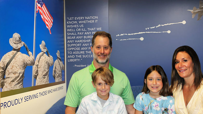 Family of four smiles in front of veterans mural in new veterans lounge