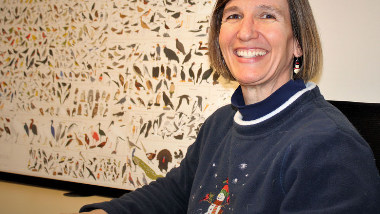 Dr. Meg Hatch seated in front of a chart depicting bird species