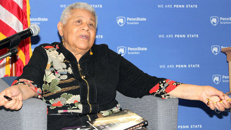 Minniejean Brown Trickey seated onstage in a chair, speaks to the crowd