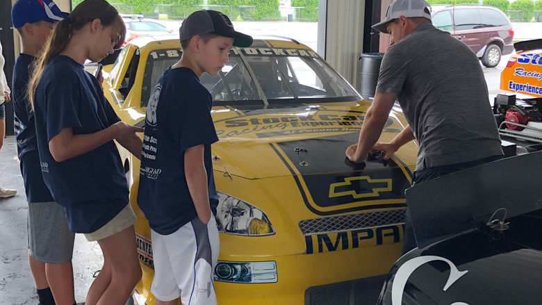 three students and an instructor surround a racecar in a garage