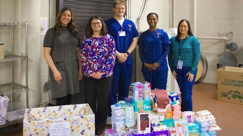 students pose near pile of donated items for baby drive
