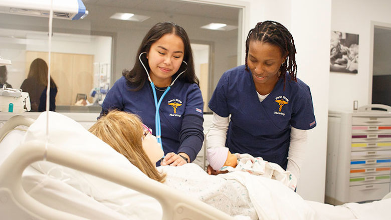 two students in scrubs use stethoscope to get vital signs on a patient simulator
