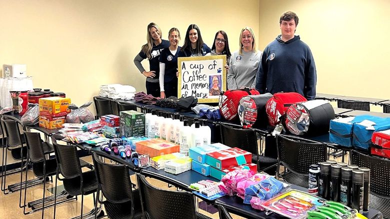 Nursing students standing behind  tables containing items they donated to local homeless shelter