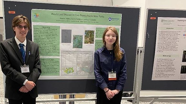 A male student at left and a female student at right stand in front of a poster titled “The Presence of Beech Leaf Disease in Two Pennsylvania State Parks.”