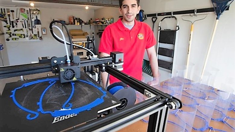 Jim Segona stands next to his 3D printer and some of the face masks he's made with it.