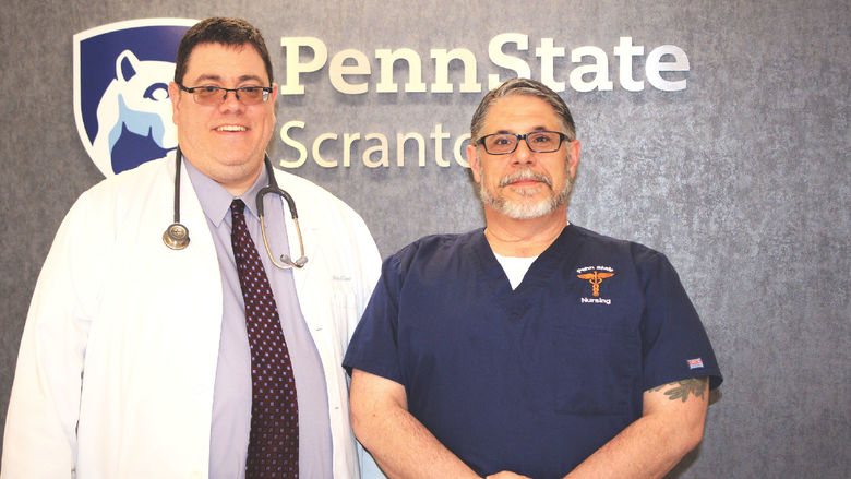photo of Mike Evans and Frank Turnbaugh standing in front of wall with Penn State Scranton campus logo