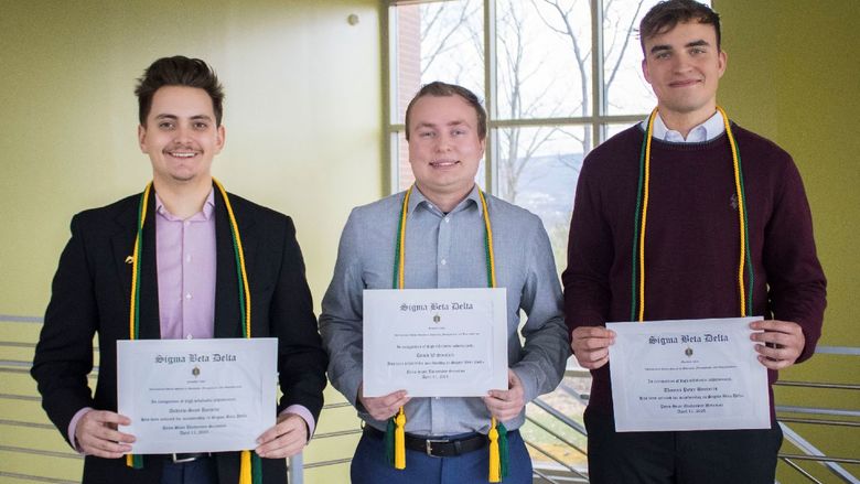 three students show off their honor society certificates, cords and pins