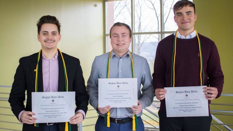 three students show off their honor society certificates, cords and pins