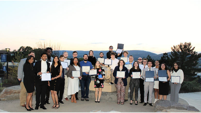group of student award winners pose for photo at campus lion shrine at sunset
