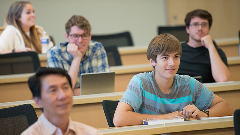 students in lecture classroom setting smile and while listening to presenter