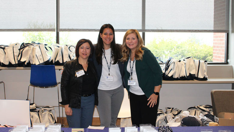 three women stand at check-in table at conference