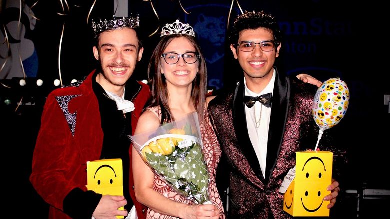 Three Student THON dancers wearing crowns and formal wear and holding yellow flowers pose for a photo after being announced at the THON Prom