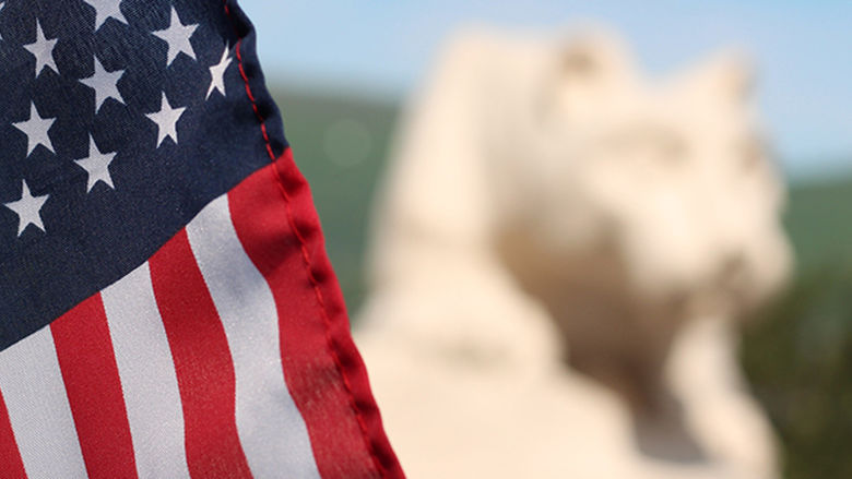 The American Flag with the campus lion shrine in the background