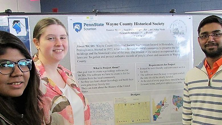 three students stand next to their research poster at a past fair event