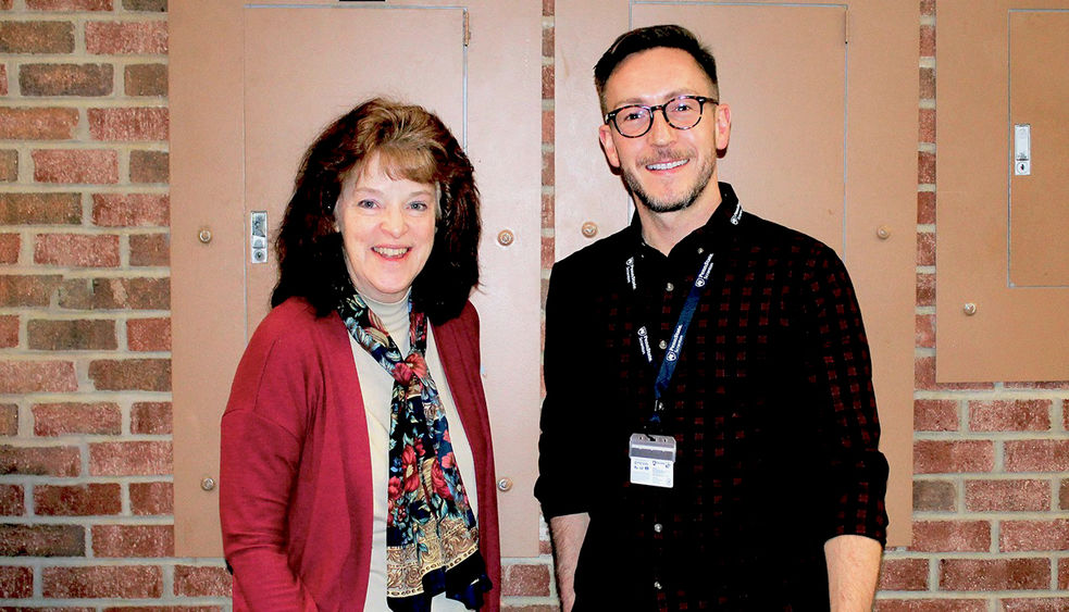 Eileen Giovagnoli and Matthew Smith stand together for a photo in the Study Learning Center with a brick wall behind them in the background