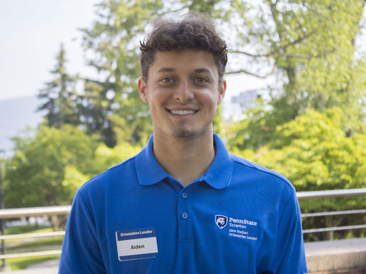 Student wearing a shirt that reads 'New Student Orientation' smiles for photo