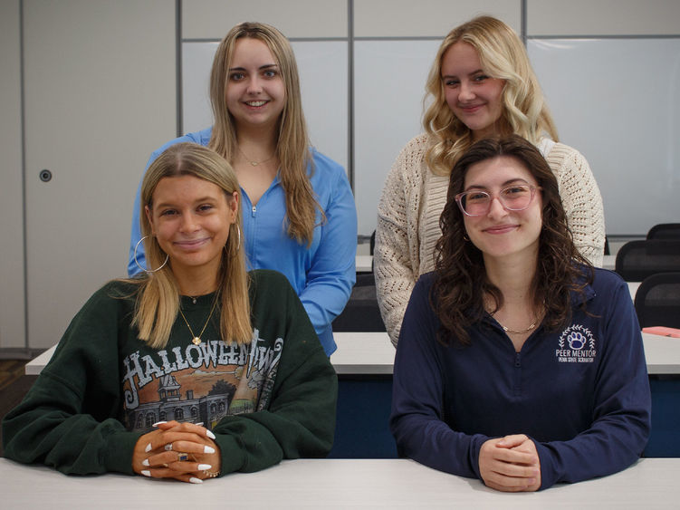 group of four students posing in a classroom for group photo