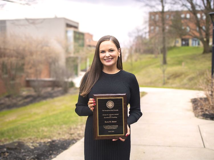 Kara Stone poses outside fo the library building with her award plaque