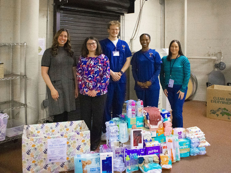 students pose near pile of donated items for baby drive