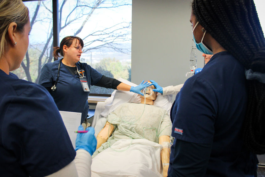 professional and student nurses gather around a patient simulator in the campus' patient simulator lab.