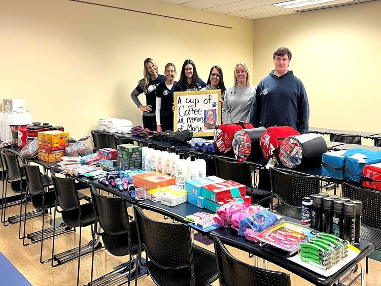 Nursing students standing behind  tables containing items they donated to local homeless shelter