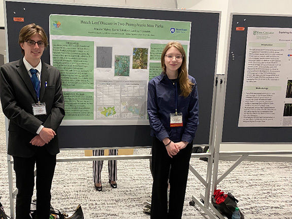 A male student at left and a female student at right stand in front of a poster titled “The Presence of Beech Leaf Disease in Two Pennsylvania State Parks.”