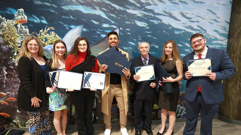 group of students pose in front of aquarium holding their award certificates
