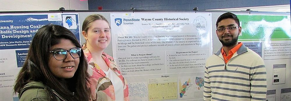 three students stand next to their research poster at a past fair event