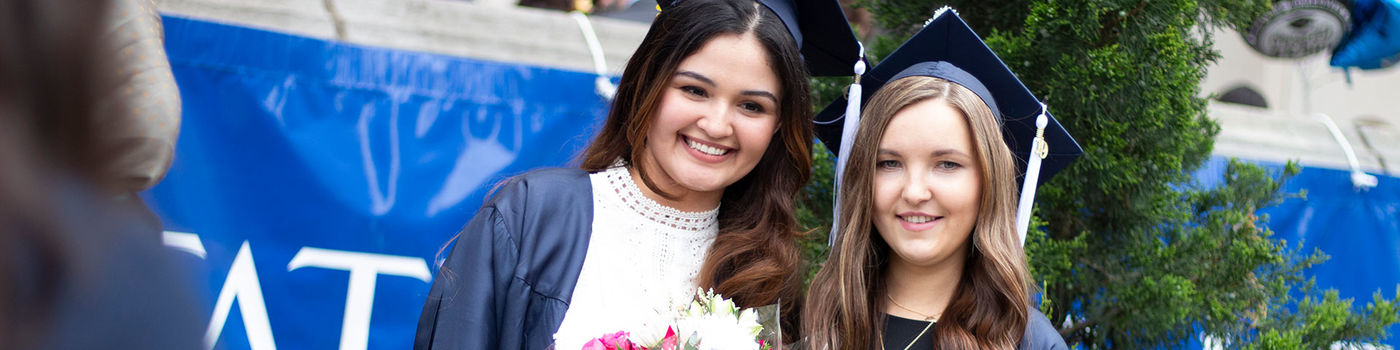 two smiling girls in caps and gowns holding diplomas